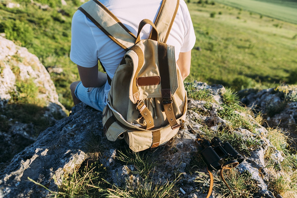 rear-view-man-with-backpack-sitting-rock-min