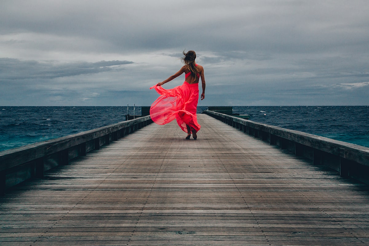 view-woman-long-pink-dress-walking-pier-windy-day-min